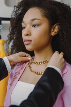 Fashion stylist adjusting a chunky chain necklace on a stylish woman indoors.