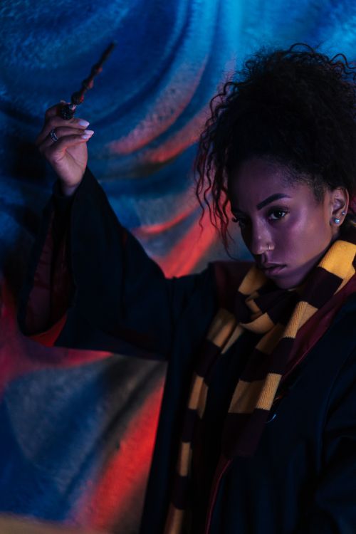 Free A woman in a wizard costume holds a wand against a colorful, mystical backdrop. Stock Photo
