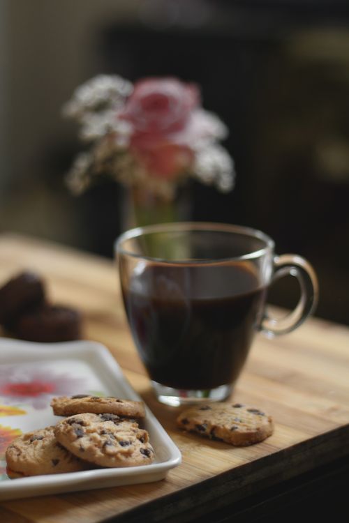 Free A glass cup of black coffee with chocolate chip cookies on a wooden table, perfect for breakfast. Stock Photo