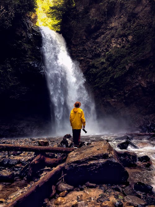 A Man in Yellow Jacket Standing Near the Waterfall