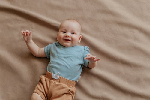 Baby in Green Shirt Lying on Brown Textile
