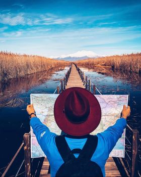 Adventurer with map on a bridge path over a serene water landscape under a clear blue sky.