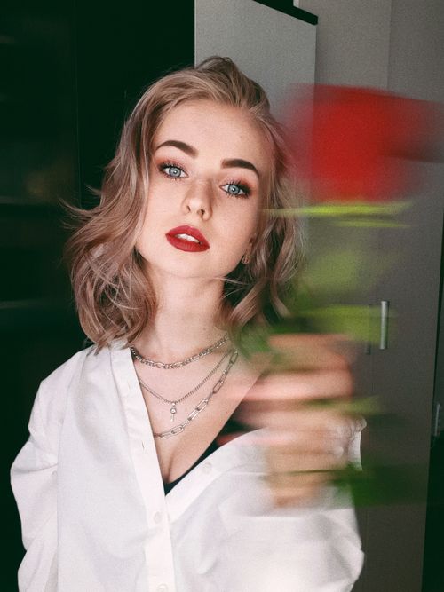 Free Portrait of a stylish woman with red lips and a white shirt holding a red rose, displaying elegance. Stock Photo