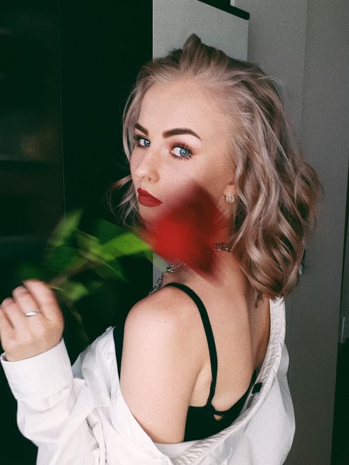 Free Portrait of a stylish young woman holding a red rose, wearing a white shirt and black bra indoors. Stock Photo