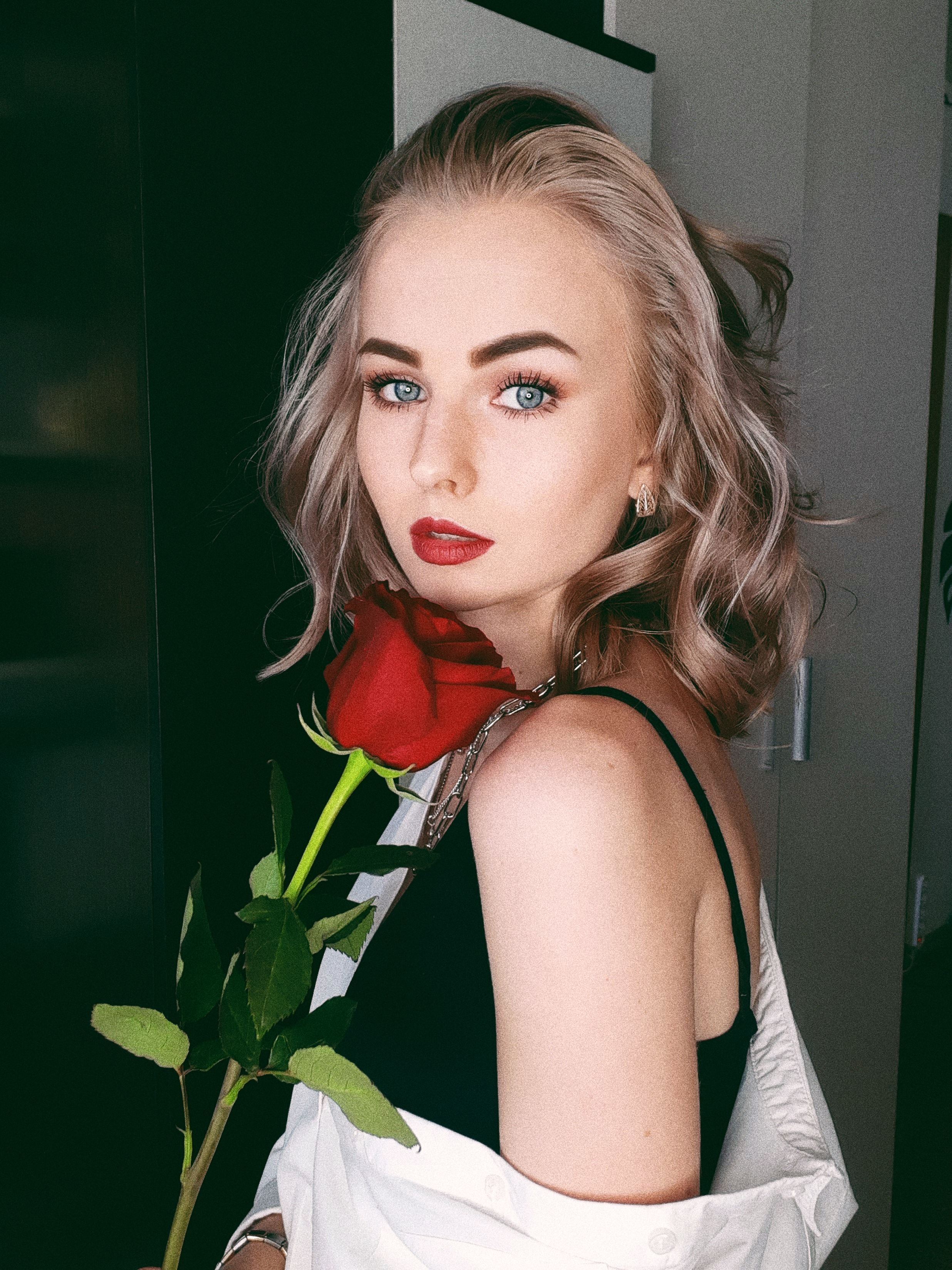 Portrait of a stylish woman with red lips and a rose in hand, conveying elegance.