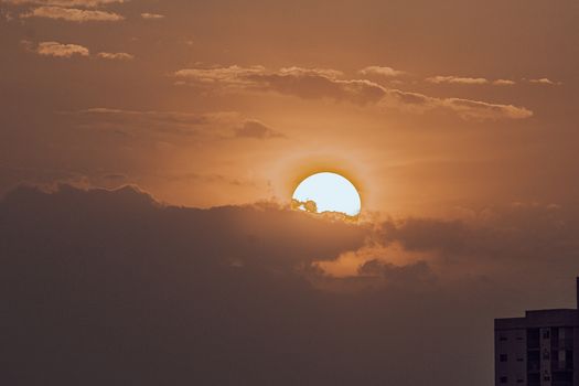 A breathtaking view of the sun setting behind clouds, casting a warm glow over a distant city skyline.