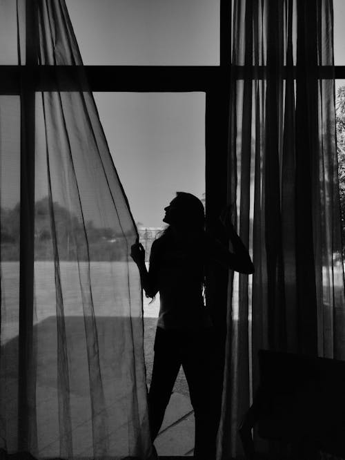 Monochrome Photo of a Woman's Silhouette Touching Curtains