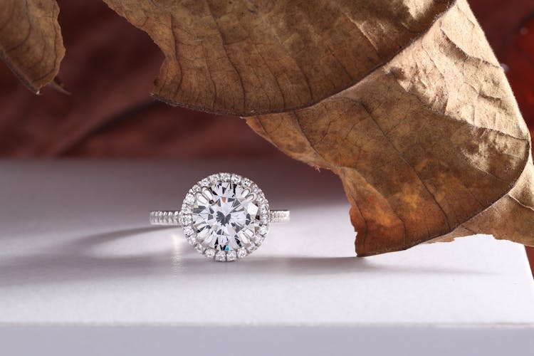 A Diamond Ring On The White Table Top With Dry Leaf