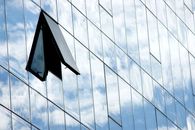 A modern glass building facade with an open window reflecting the cloudy sky in Brașov, Romania.