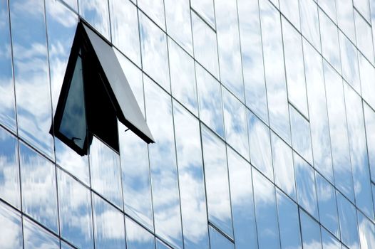 A modern glass building facade with an open window reflecting the cloudy sky in Brașov, Romania.