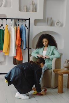 Two women in a boutique trying on shoes surrounded by vibrant clothing on a rack.
