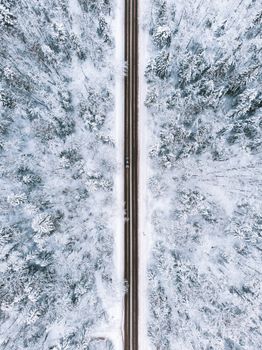 Drone shot of a road cutting through a snow-covered forest in winter, showcasing nature's beauty from above.