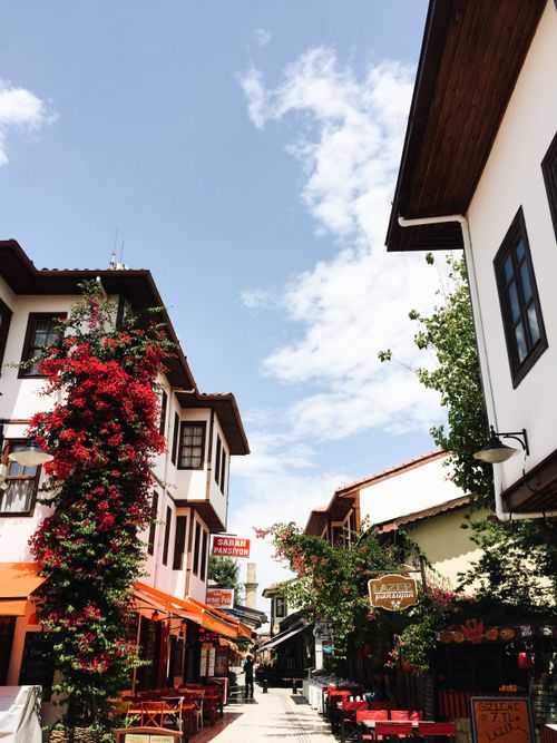 Free Narrow street with residential houses decorated with blooming plants and street cafes with chairs and tables in old town on sunny day in summer Stock Photo