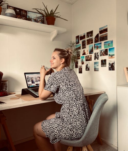 Woman in Black Floral Dress Sitting on Table with Laptop