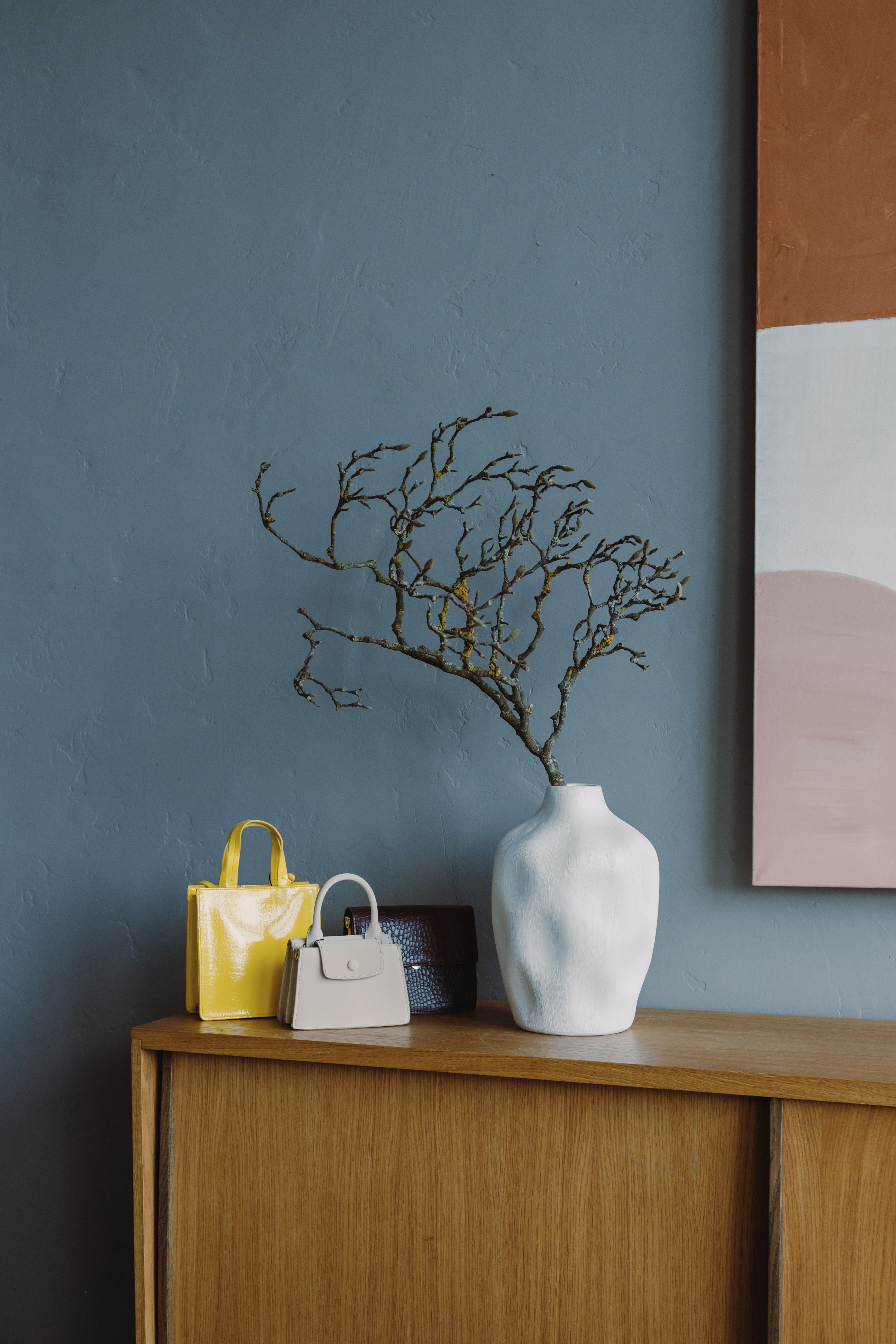 Cortile satchel in a minimal interior beside a branch-filled vase