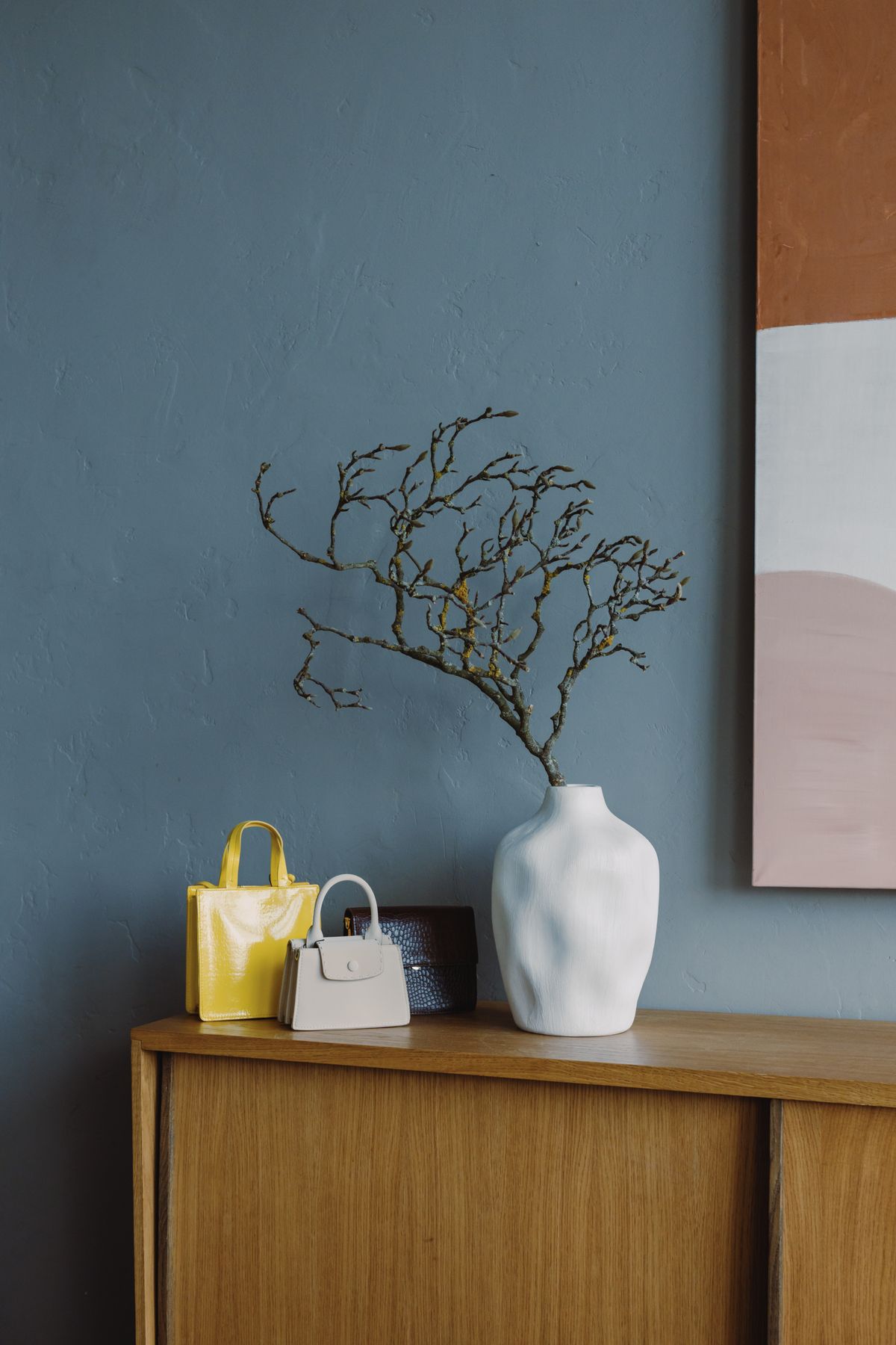 Cortile satchel in a minimal interior beside a branch-filled vase