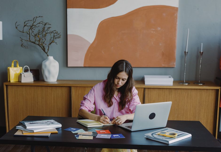 Woman working remotely at home office on a design project with laptop and color swatches.