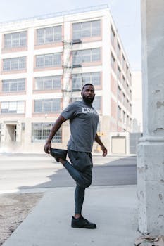 African American man stretching his leg in an urban street setting, emphasizing healthy lifestyle and fitness.