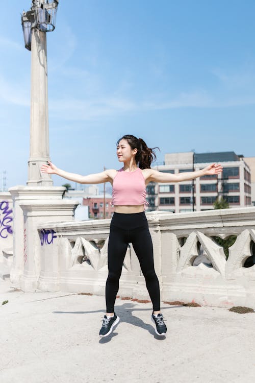 Free Woman Wearing Pink Crop Top Jumping on Concrete Floor Stock Photo