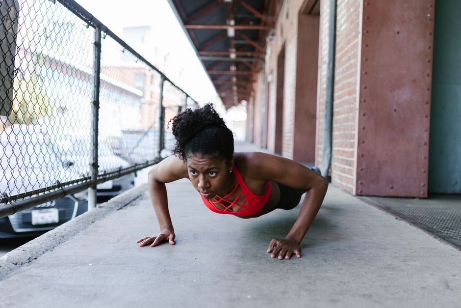 Focused woman in activewear doing push-ups outdoors against a brick wall.