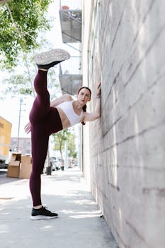 A woman in fitness attire stretches on a city sidewalk, demonstrating flexibility and strength.
