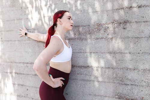 Free Fitness woman stretching against a sunlit concrete wall wearing activewear. Stock Photo