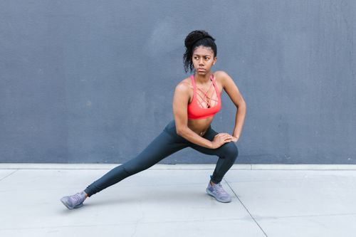 Free A woman in sportswear stretching against a gray wall, symbolizing fitness and health. Stock Photo