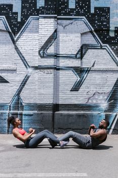 A fit couple performs ab workouts against a graffiti wall outdoors, showcasing urban fitness.