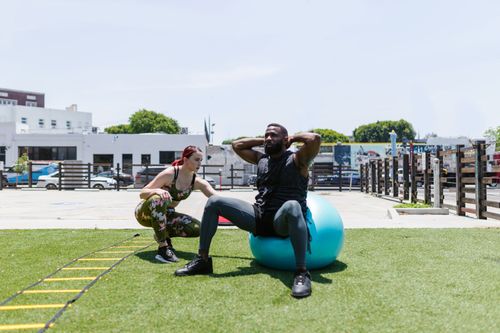 Free Man and woman engaged in fitness activities outdoors using an exercise ball. Stock Photo