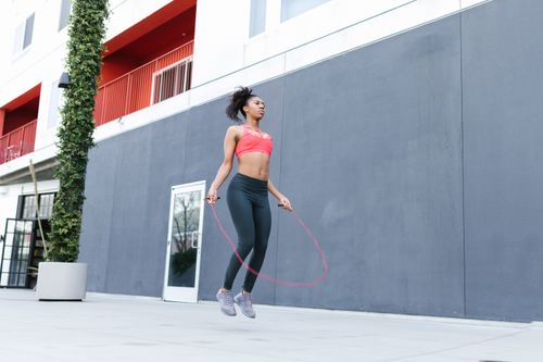 Free Fit woman with curly hair exercising outdoors by skipping rope. Focus on fitness and motion. Stock Photo