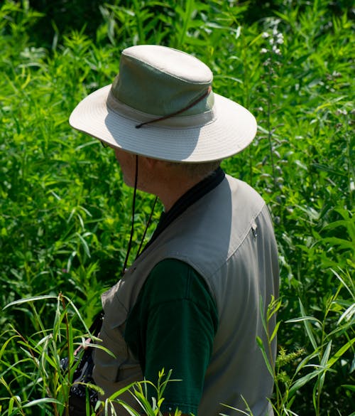 Man in Gray Vest and Hat Standing Beside Plants