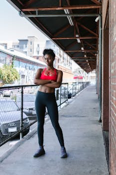 Confident young woman in sportswear standing on a city street, embracing fitness and lifestyle.