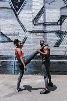 Two people practicing calisthenics and fitness outdoors against an urban mural backdrop.