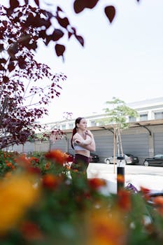 Woman in activewear thinking during outdoor workout, surrounded by vibrant blooms.