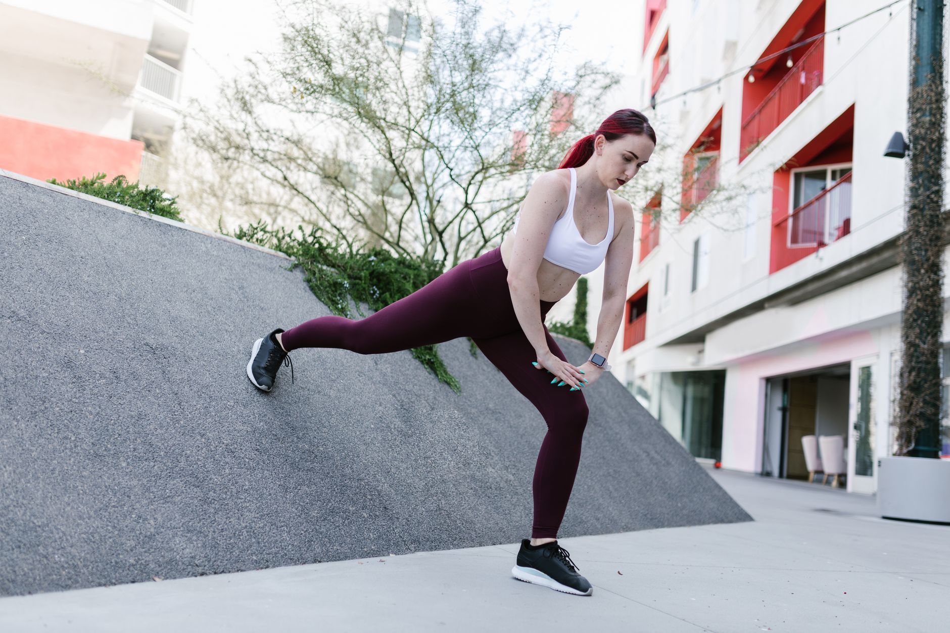 A woman wearing activewear stretches on a ramp in an outdoor urban setting, promoting fitness.