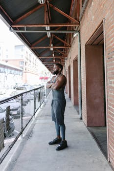 Man in sportswear stands confidently by a city brick wall, showcasing fitness and style.