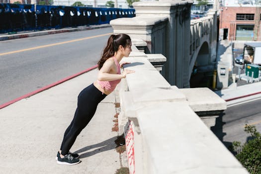 A woman performs a workout on a bridge railing in a sunny cityscape.