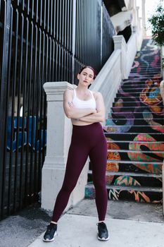 A woman wearing activewear poses confidently in front of colorful street art stairs outdoors.
