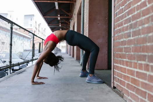 Woman practicing a backbend yoga pose outdoors against a brick wall, promoting wellness and healthy living.
