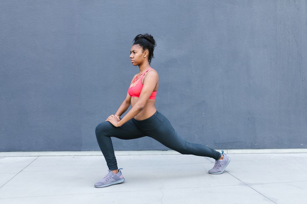 Woman performing a lunge stretch against a gray wall