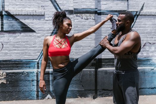 A woman and a man performing a stretching exercise together in an urban setting.
