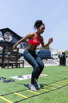 A fit woman exercising outdoors using an agility ladder for strength and speed training.