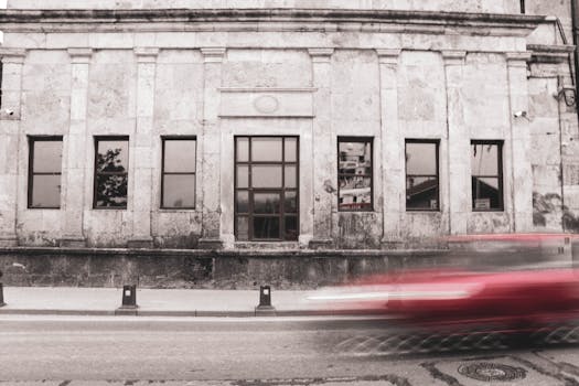 Grayscale image of an old building facade with a red car's motion blur, capturing urban life in Istanbul.