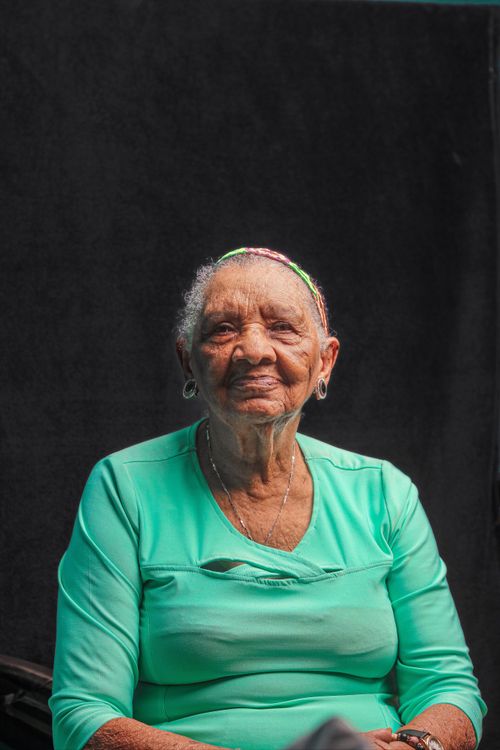 Free Close-up portrait of a smiling senior woman wearing a green top against a dark background. Stock Photo