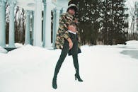 一位穿着迷彩夹克和靴子的时尚女子在雪地里摆姿势