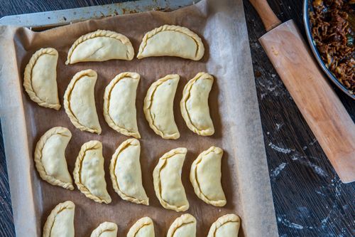 Free Raw homemade empanadas arranged on a baking tray, viewed from above, ready to be cooked. Stock Photo