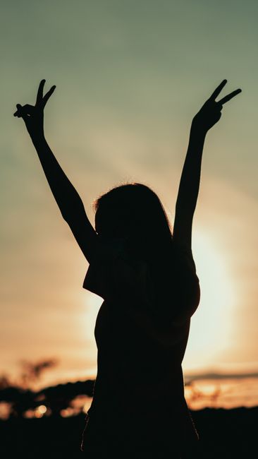 Fotomural Silueta de una mujer levantando las manos en señal de paz durante el atardecer, simbolizando libertad y tranquilidad.