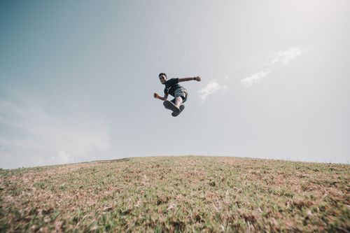 Free Dynamic shot of a man jumping joyfully on a grassy hill under a clear sky, capturing a moment of freedom. Stock Photo
