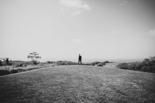 Grayscale Photo of Man Standing on Grass Field
