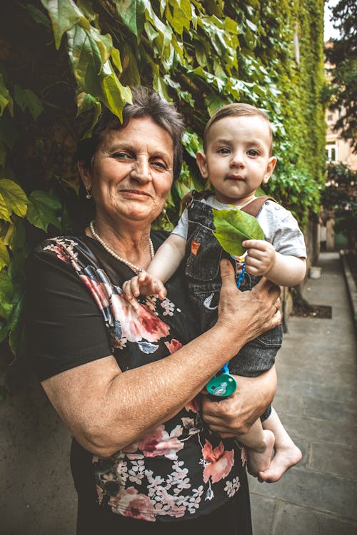 Woman in Floral Shirt Carrying a Baby Boy in Denim Jumper 